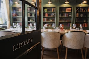 A library with bookshelves, a table set for dining, and chairs. - The George & Dragon (Westerham)