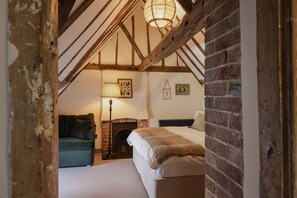A bedroom with a sloped ceiling, exposed wooden beams, a fireplace, a sofa, and a bed.