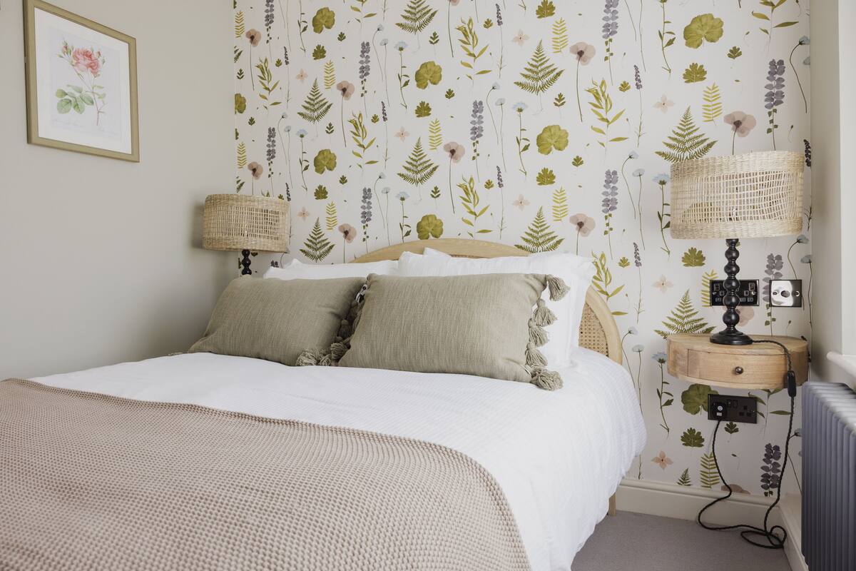 A bedroom with a bed, two bedside lamps, a nightstand, and a wall-mounted power outlet.