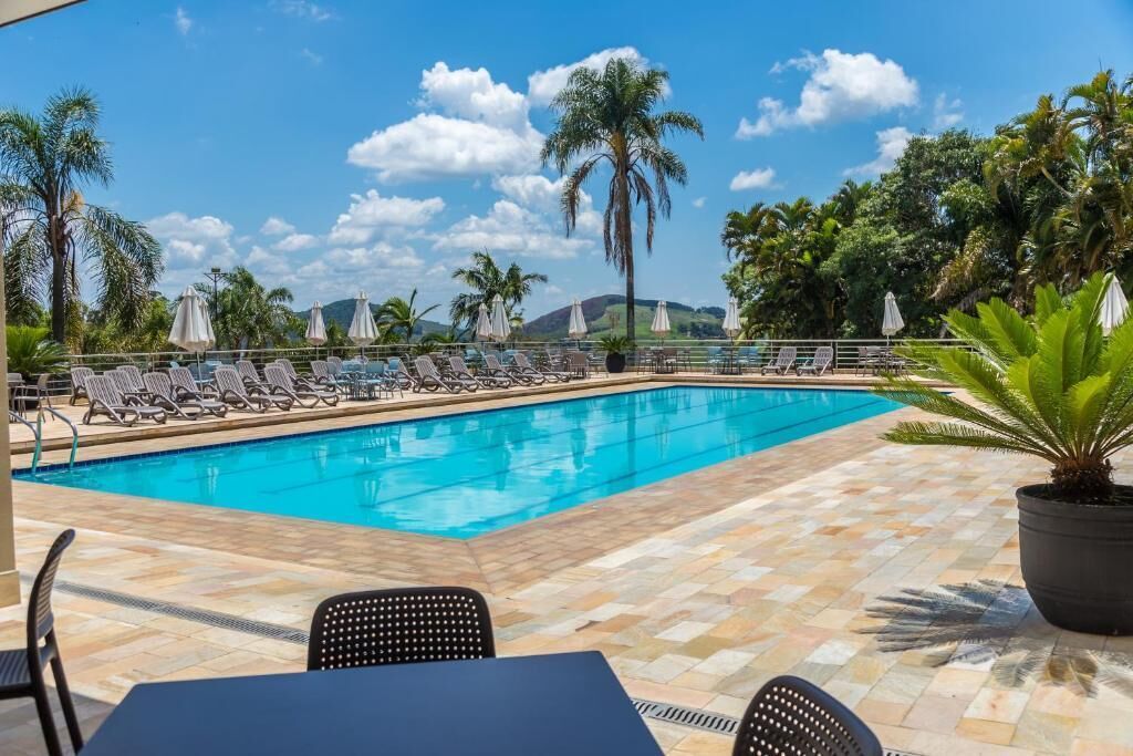 A pool area with lounge chairs and umbrellas, surrounded by palm trees and a clear sky.