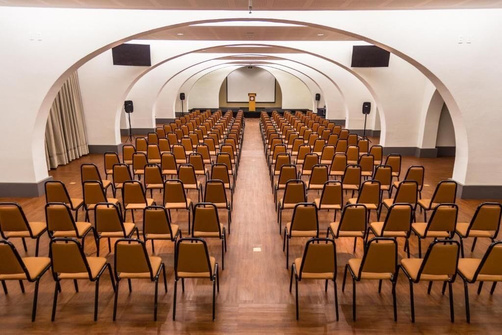 A conference room with rows of chairs facing a stage with a podium and a screen.