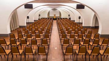 A conference room with rows of chairs facing a stage with a podium and a screen.