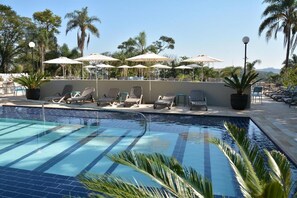 A swimming pool with lounge chairs and umbrellas, surrounded by palm trees and a clear sky.