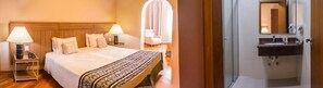A hotel room with a bed, bedside lamps, a bedside table, a bathroom with a sink and mirror.