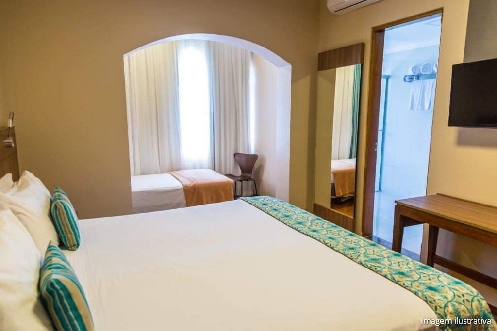 A hotel room with a large bed, a small desk, a chair, and a mirror.