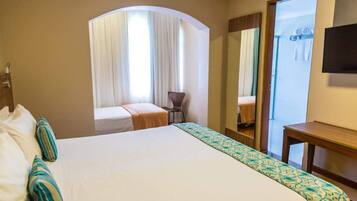 A hotel room with a large bed, a small desk, a chair, and a mirror.