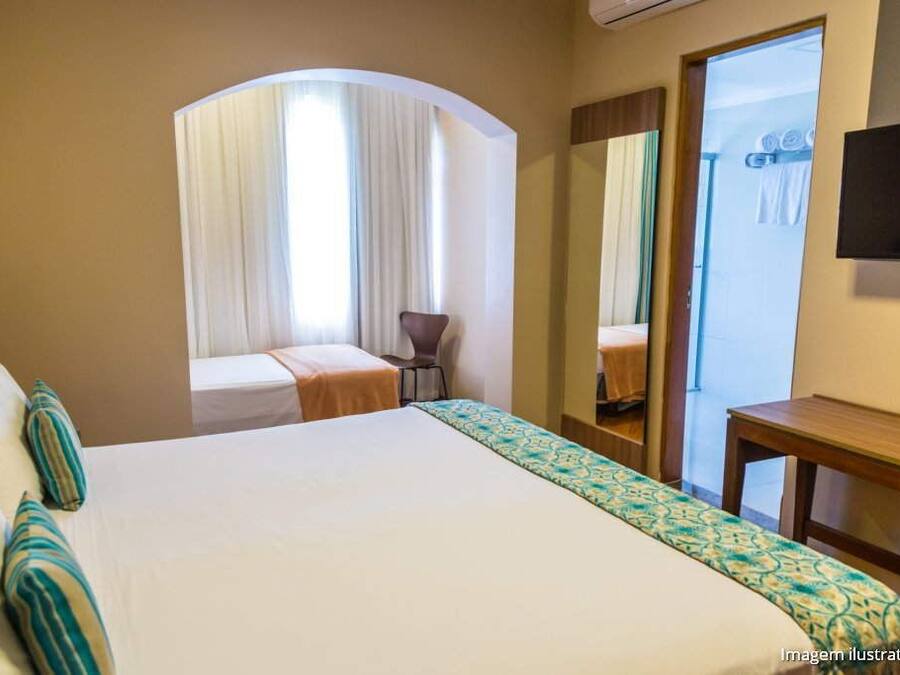 A hotel room with a large bed, a small desk, a chair, and a mirror.