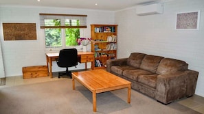 A living room with a wooden desk, a brown sofa, a wooden coffee table, and a bookshelf.