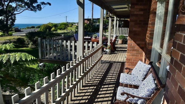 A balcony with a white picket fence, two patterned chairs, and a view of the ocean and greenery.