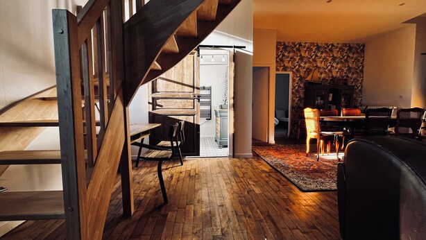 A modern interior with a wooden staircase, a dining area with a patterned wall, and a living room with a sofa and chairs. - Old school in the heart of a village near Puy du Fou (Sèvremoine)