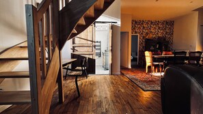 Een modern interieur met een houten trap, een eetgedeelte met een behangwand en een woonkamer met een bank en stoelen.