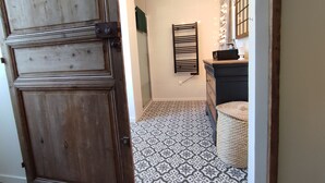A hallway with patterned floor tiles, a wooden door, a dark-colored dresser, and a mirror with lights. - Old school in the heart of a village near Puy du Fou (Sèvremoine)