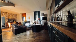A modern living room with a sofa, a coffee table, and a TV. There is a kitchen area with a countertop and cabinets. - Old school in the heart of a village near Puy du Fou (Sèvremoine)