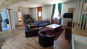A spacious living room with a wooden floor, a sofa set, a coffee table, and a television. - Old school in the heart of a village near Puy du Fou (Sèvremoine)