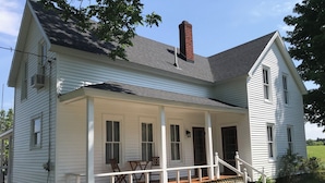 A two-story white house with a covered porch, a brick chimney, and a small garden area.