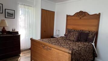 A bedroom with a wooden bed, a nightstand, a lamp, and a window with sheer curtains.