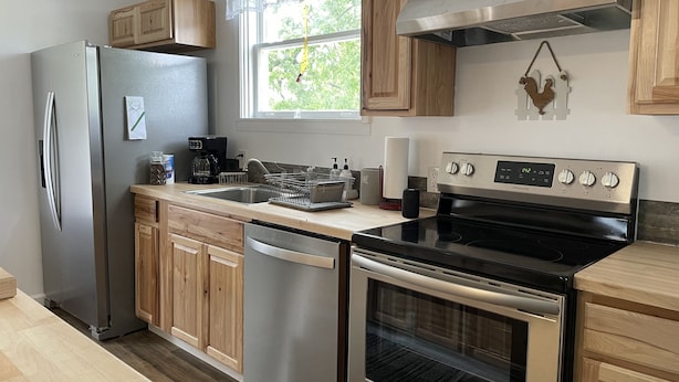 A modern kitchen with stainless steel appliances, wooden cabinets, and a window providing natural light.