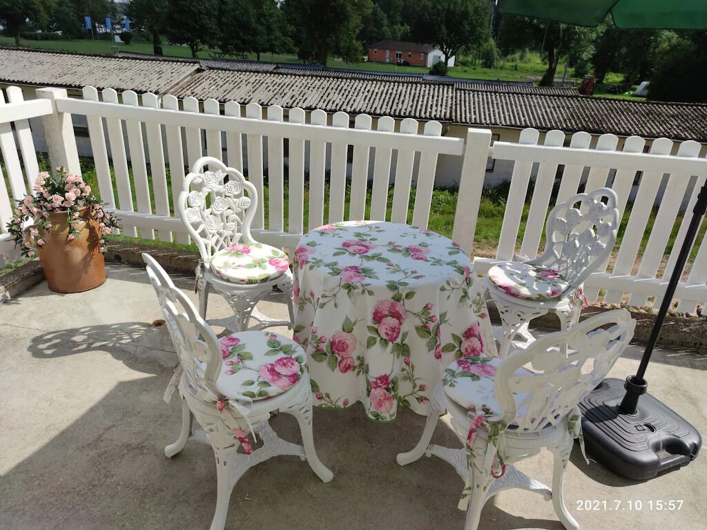 Eine Terrasse mit einem runden Tisch, vier Stühlen, einem weißen Zaun und einem Blumentopf.