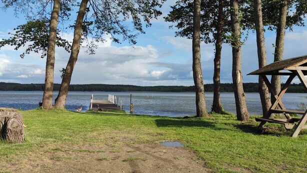 A lakeside campsite with a wooden deck, picnic table, and shelter.