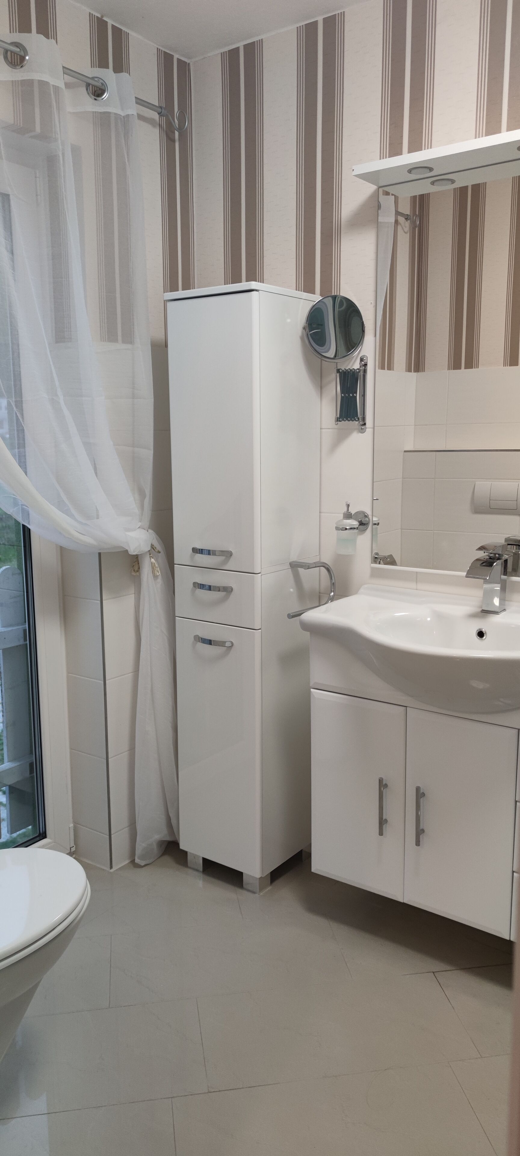 Ein Badezimmer mit Toilette, Waschbecken, Spiegel und Duschbereich.