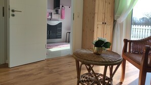 A room with a wooden floor, a wicker chair, a small table with a plant, and a wardrobe.