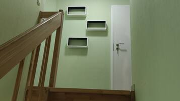 Eine Treppe mit hölzernen Geländern führt zu einer Tür mit Schlüsselloch. An der Wand befinden sich drei weiße, rechteckige Stauraumfächer.