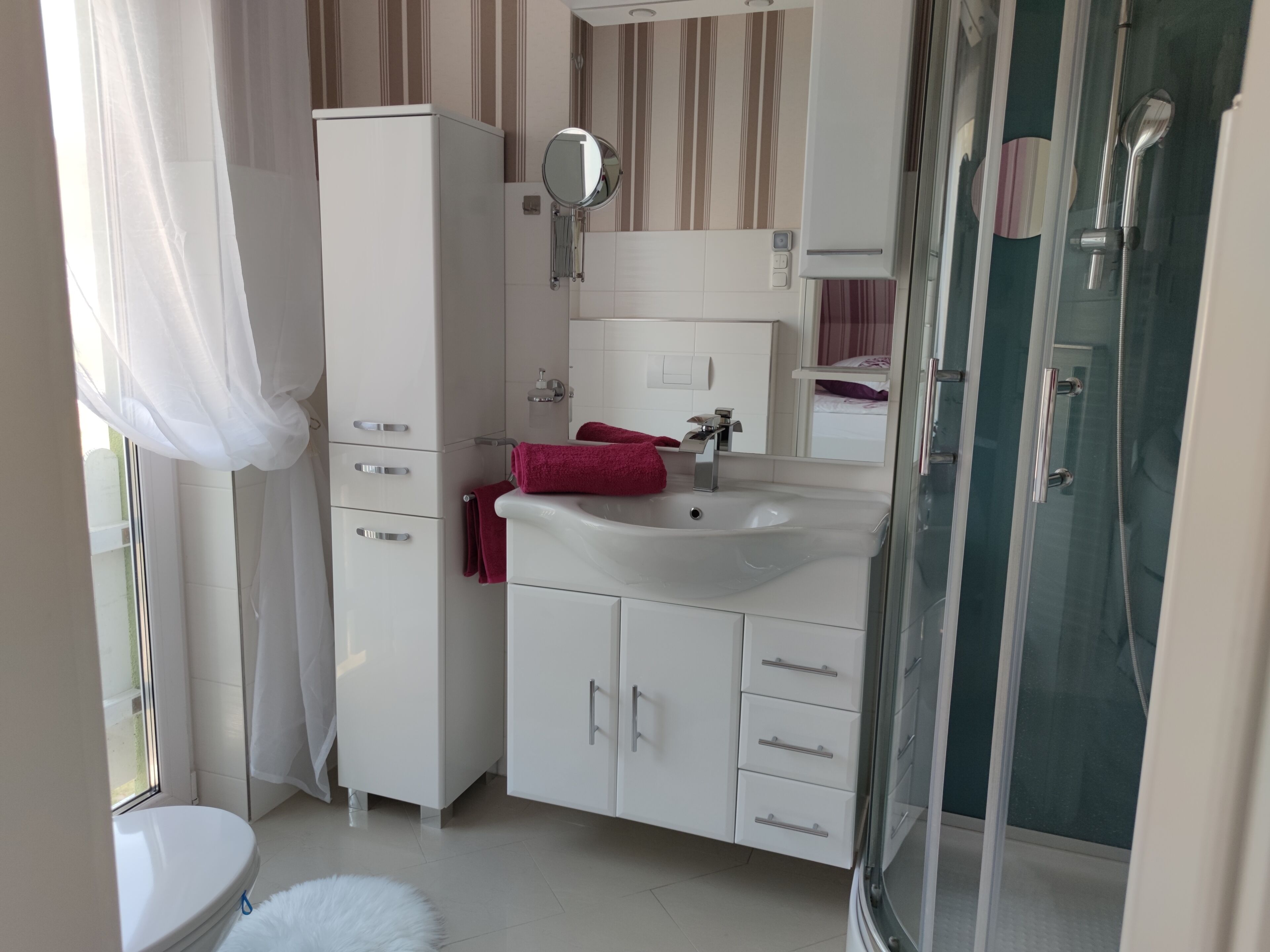 A bathroom with a toilet, a sink, a mirror, a shower, and a wardrobe.