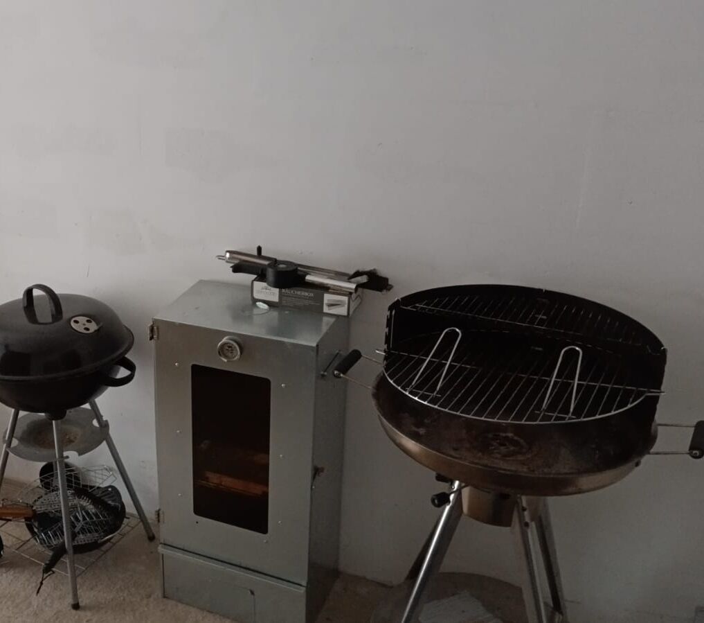 Une cuisinière à gaz portable et un barbecue à charbon placés contre un mur uni.