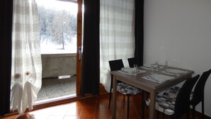 A dining area with a table set for four, a sliding glass door leading to a balcony, and a view of trees outside.