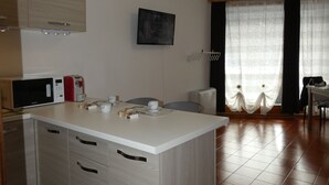 A modern kitchen with a central island, a microwave, a toaster, and a sink. There is a television mounted on the wall and a window with curtains.