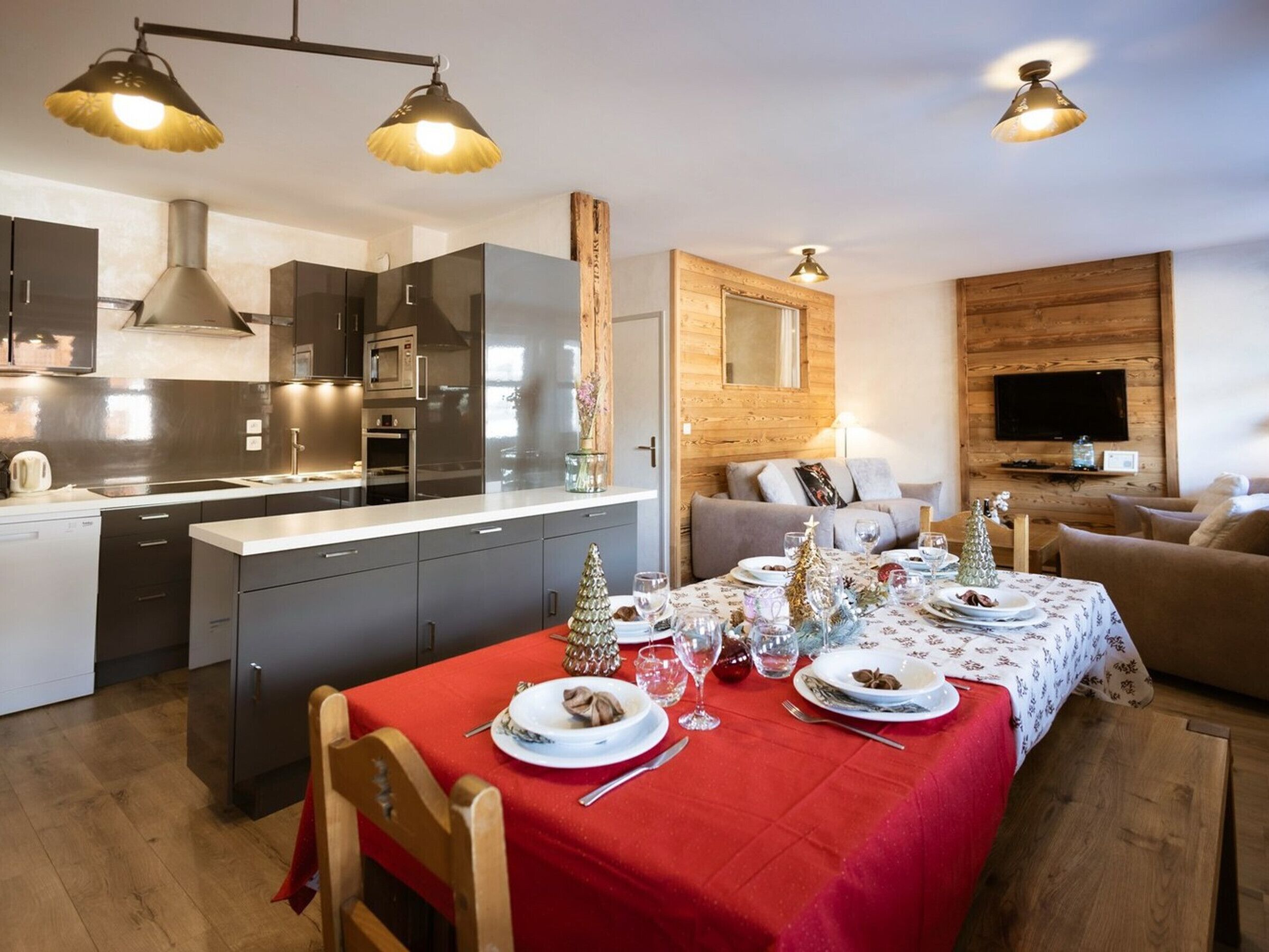 Een moderne keuken met roestvrijstalen apparatuur, een eethoek met een rode tafelkleed en kerstdecoraties, en een gezellige woonkamer met een flatscreen-televisie.
