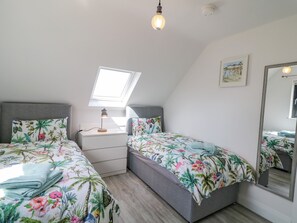 A bedroom with two beds, a skylight, a bedside lamp, a small table, and a mirror.