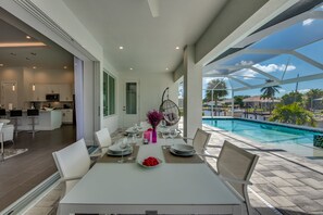 A modern dining area with a pool view, white furniture, and a hanging chair. - Villa Seven Oceans - stylish new villa, extra large pool & spa, boat dock (Cape Coral)