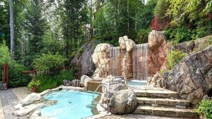 Zona de piscina exterior con diseño natural, que incluye una cascada, rodeada de rocas y vegetación.