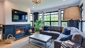 Una sala de estar moderna con chimenea, un sofá grande, una mesa de centro y un televisor montado en la pared.