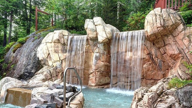 Una poza natural de roca con cascada, rodeada de rocas y vegetación.