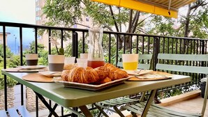 An outdoor dining area with a table set for breakfast, including croissants and a pitcher of juice, under a striped canopy. - Charmant et Spacieux Appartement T3 en Bord de mer (Canet-en-Roussillon)