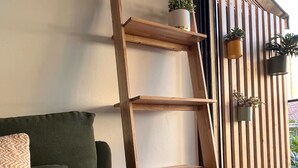 A wooden ladder shelf with potted plants, a green sofa with cushions, and a tiled floor. - Charmant et Spacieux Appartement T3 en Bord de mer (Canet-en-Roussillon)