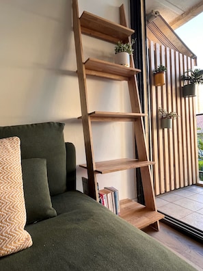 Eine hölzerne Leitereinrichtung mit Blumentöpfen, ein grünes Sofa mit Kissen und ein gefliestes Parkett.