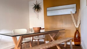 A modern dining area with a glass table, wooden benches, and a plant hanging from the ceiling. - Charmant et Spacieux Appartement T3 en Bord de mer (Canet-en-Roussillon)