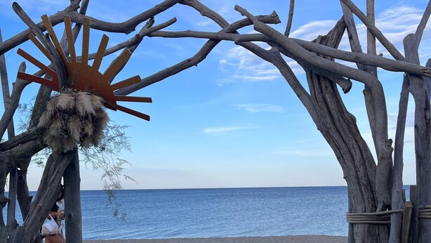 A beach scene with a rustic wooden archway, a metal chair with a striped cushion, and a sandy beach leading to the ocean. - Charmant et Spacieux Appartement T3 en Bord de mer (Canet-en-Roussillon)