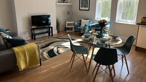 A modern living room with a sofa, TV, dining table, chairs, and a blue floral sofa. - Between the beach and the shops (Portsmouth)
