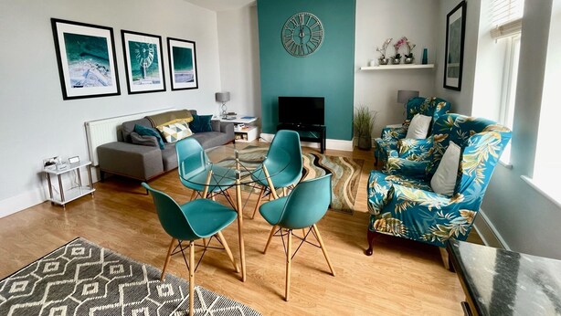 A modern living room with a sofa, teal chairs, a coffee table, a fireplace, and wall art. - Between the beach and the shops (Portsmouth)