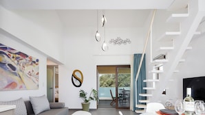 A modern living room with a sofa, a dining table set for two, and a staircase. - Coconut Palm Paradise (Rethymno)