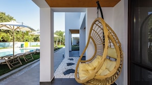 A modern interior with a hanging chair, a pool area, and a pathway leading to a covered outdoor space. - Coconut Palm Paradise (Rethymno)