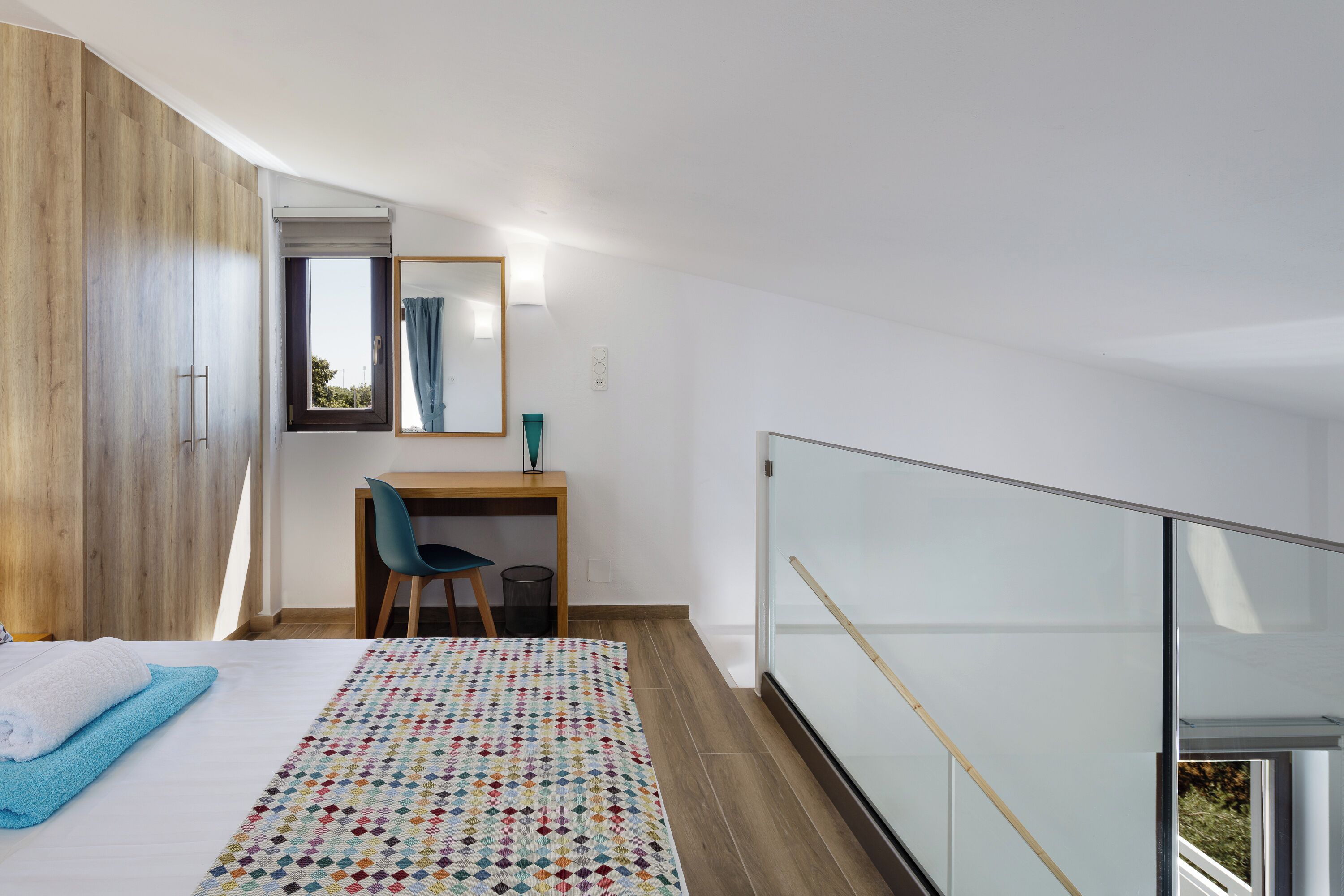 A bedroom with a bed, a desk, and a window.