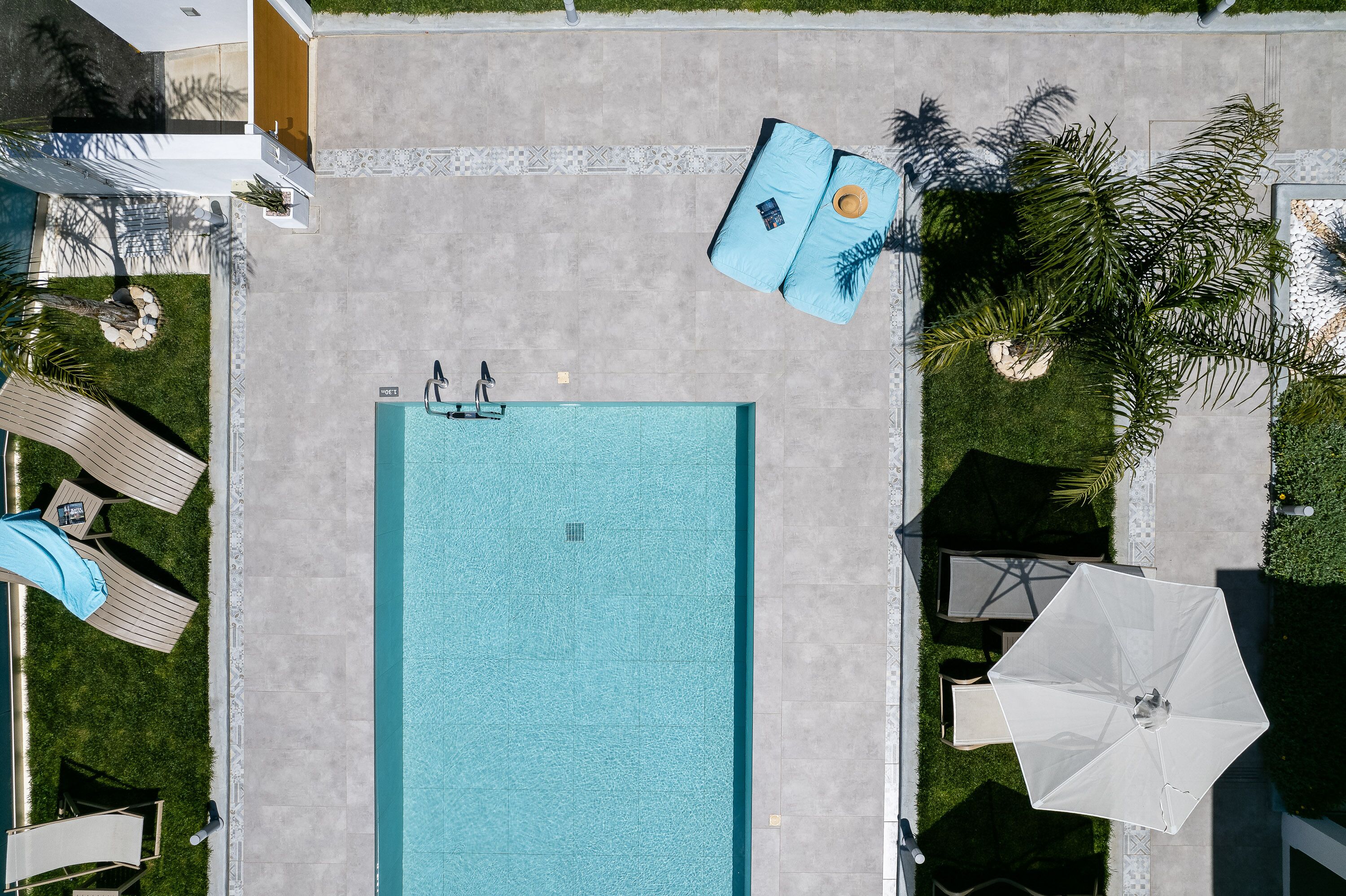 An aerial view of a swimming pool area with lounge chairs, a poolside umbrella, and a small garden with palm trees.
