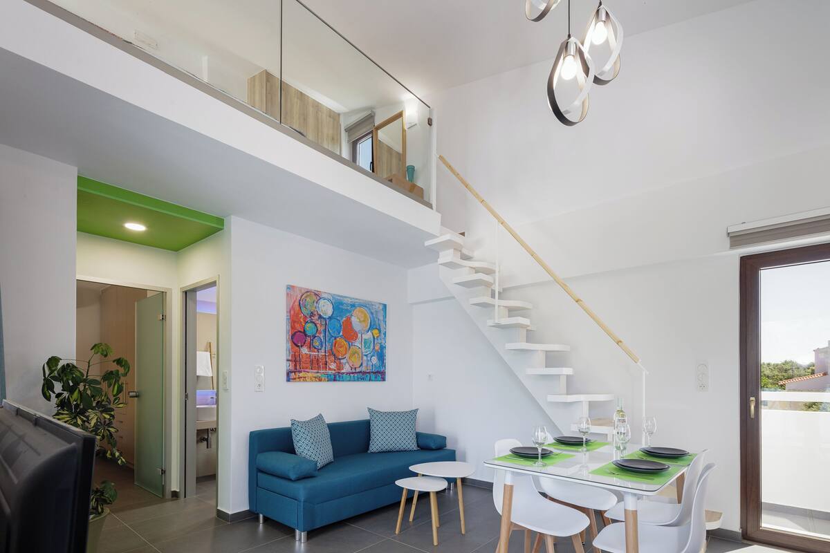 En moderne stue med blå sofa, spisebord med stole, trappe og et stort vindue.