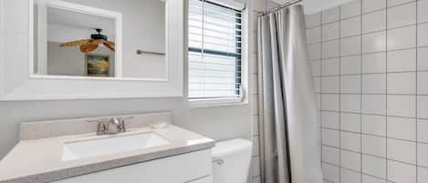 A bathroom with a white sink, a toilet, a shower with a curtain, and a window with blinds.