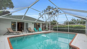 A swimming pool with a covered patio area, outdoor furniture, and a view of palm trees. - A Quaint and Serene Neighborhood in North Naples (Naples)